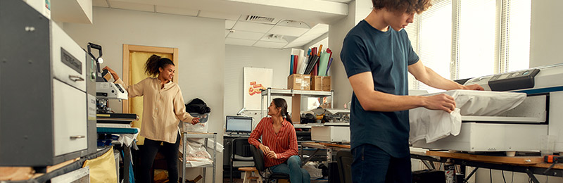 Two female and two male entrepreneurs working in a small office on taking and fulfilling online orders. One is reviewing their business plan to see if their eCommerce site is on track.